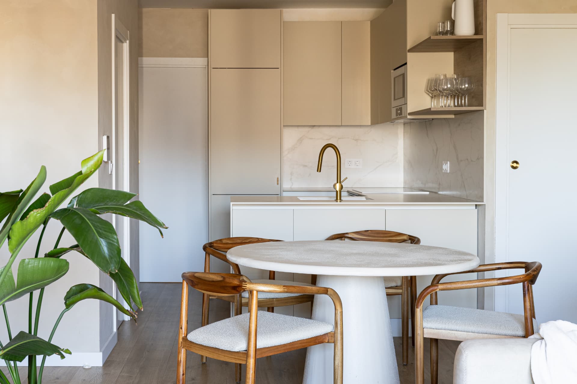 Kitchen and dining area with round stone table, wooden armchairs and brass faucet